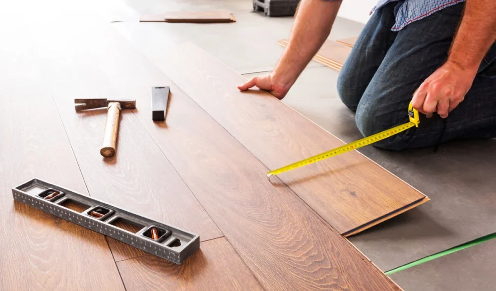 Hands of a carpenter fitting engineered wood floor panels together e1779620740806